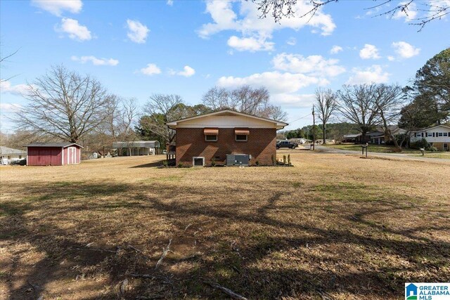 exterior space with brick siding, a storage shed, a lawn, and an outbuilding