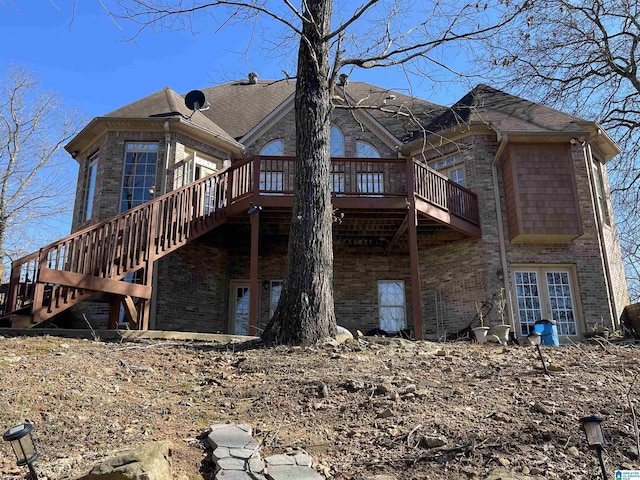 rear view of property with a deck, stairway, brick siding, and a shingled roof