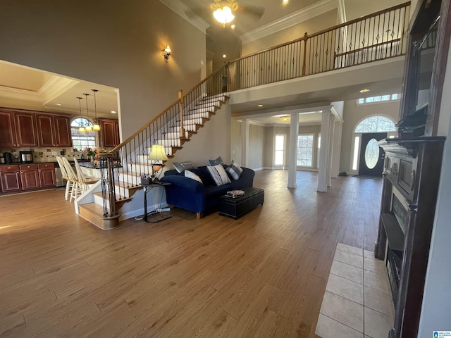 living room with plenty of natural light, light wood-style flooring, stairs, and crown molding