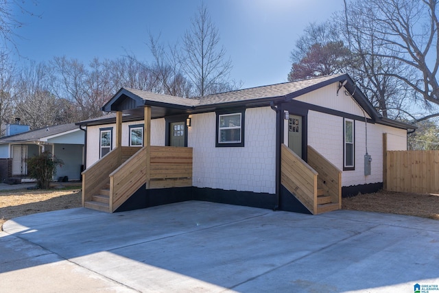 view of front of property featuring fence, concrete driveway, and roof with shingles