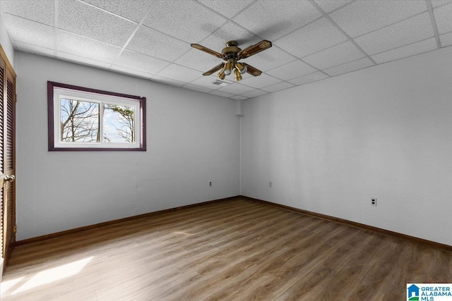 empty room featuring a drop ceiling, visible vents, baseboards, and wood finished floors