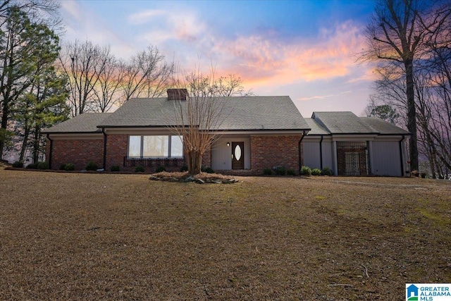 view of front of house with brick siding, a lawn, and a chimney