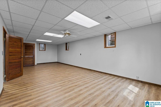 finished below grade area featuring a paneled ceiling, baseboards, visible vents, and wood finished floors