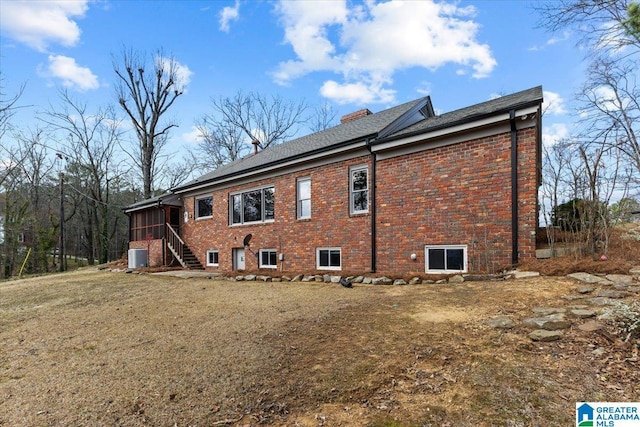 rear view of property featuring brick siding, a chimney, a sunroom, and central air condition unit