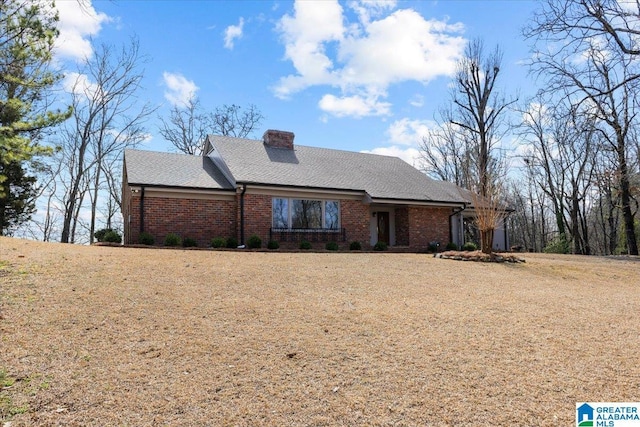 view of front facade with a shingled roof, a chimney, and brick siding