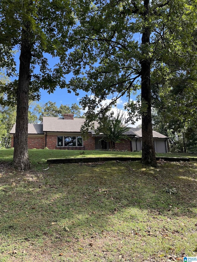 ranch-style home featuring a garage, a chimney, a front lawn, and brick siding