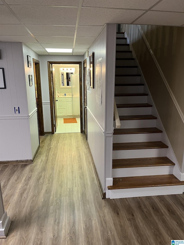 hallway with a paneled ceiling, light wood-style floors, and stairs