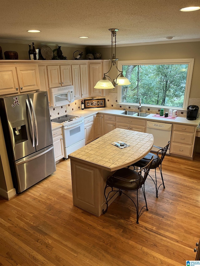 kitchen with light wood finished floors, light countertops, decorative backsplash, white appliances, and a sink