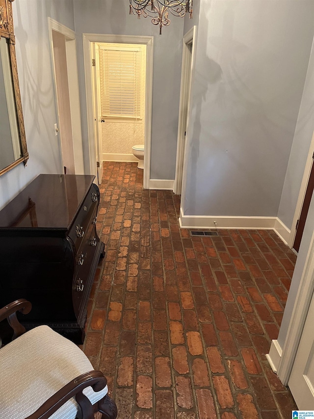 hall featuring brick floor and baseboards