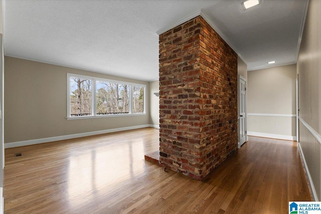 interior space with crown molding, a textured ceiling, baseboards, and wood finished floors