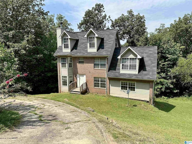 view of front of home featuring driveway, a chimney, a front lawn, and brick siding