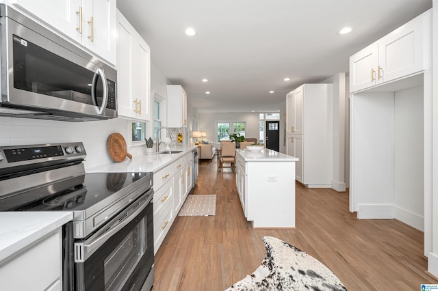 kitchen featuring light wood-type flooring, appliances with stainless steel finishes, decorative backsplash, and a sink