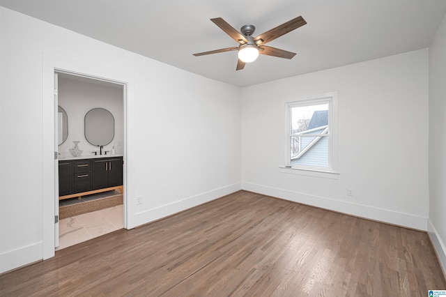 unfurnished bedroom with a sink, ensuite bath, wood finished floors, and baseboards