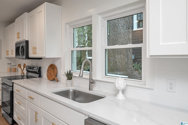 kitchen with light stone counters, decorative backsplash, appliances with stainless steel finishes, white cabinetry, and a sink