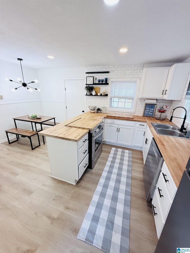 kitchen featuring stainless steel appliances, a sink, wood counters, light wood-type flooring, and decorative backsplash