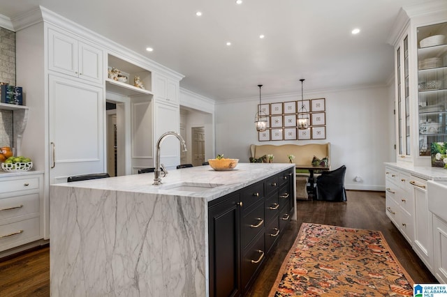 kitchen with dark cabinetry, a center island with sink, a sink, and white cabinetry