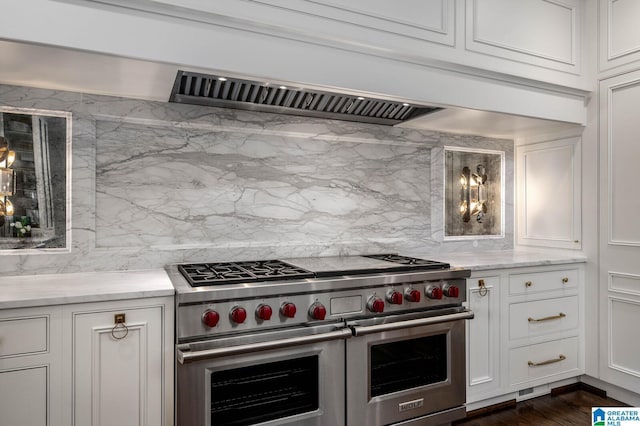 kitchen with light stone counters, white cabinetry, range with two ovens, and decorative backsplash