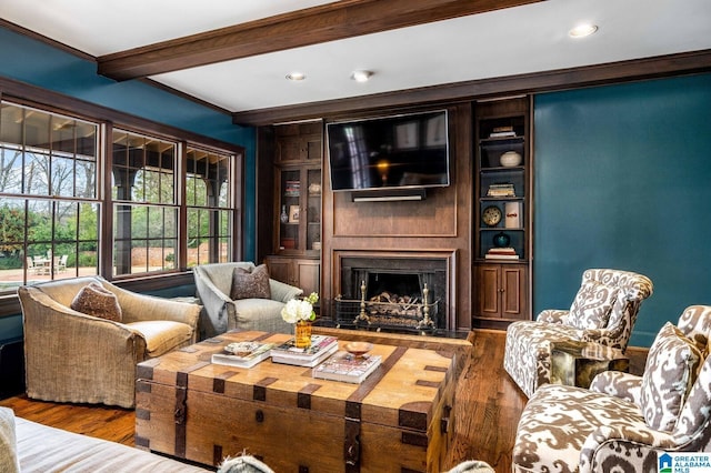 living room with built in features, ornamental molding, a large fireplace, wood finished floors, and beamed ceiling