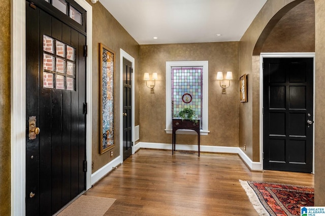 entrance foyer with arched walkways, baseboards, and wood finished floors