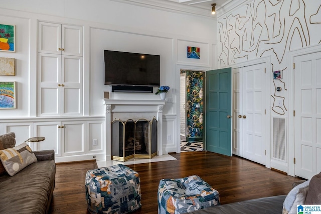 living room with dark wood-style floors, visible vents, a decorative wall, ornamental molding, and a fireplace with flush hearth