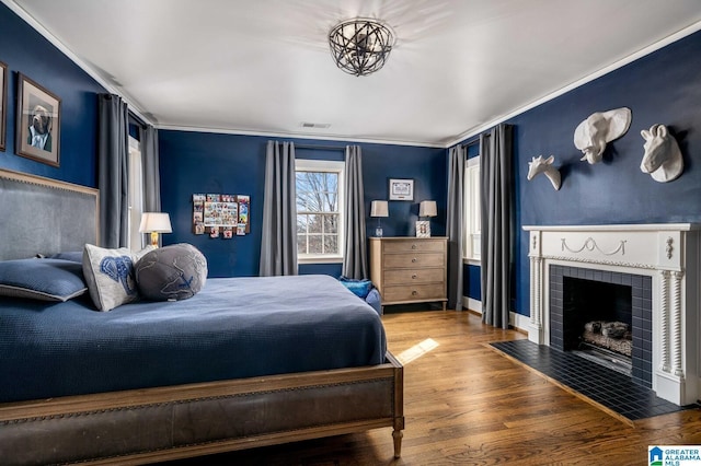 bedroom with baseboards, visible vents, wood finished floors, crown molding, and a fireplace