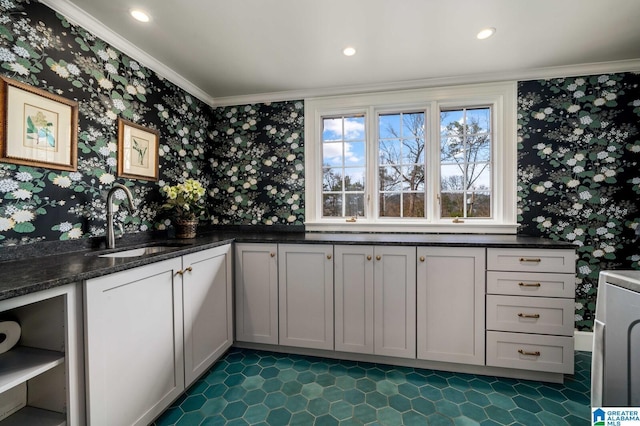 kitchen featuring wallpapered walls, dark stone counters, ornamental molding, a sink, and recessed lighting