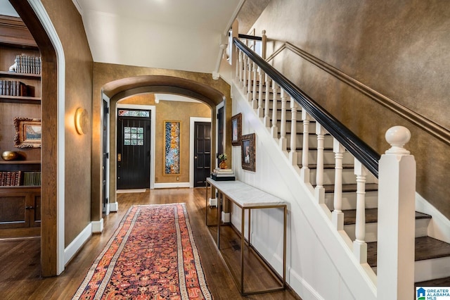 foyer entrance featuring arched walkways, wood-type flooring, baseboards, and stairs