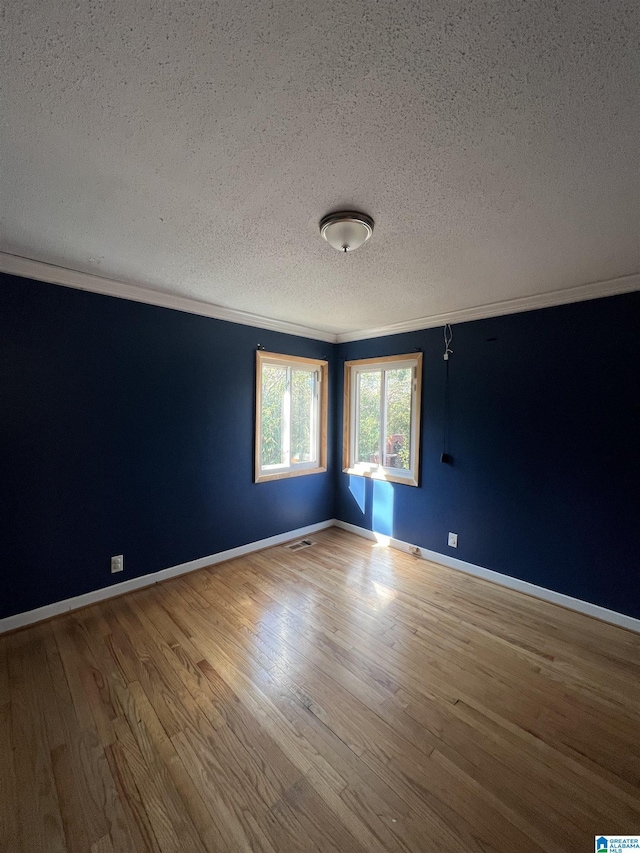 spare room with a textured ceiling, ornamental molding, wood finished floors, and baseboards