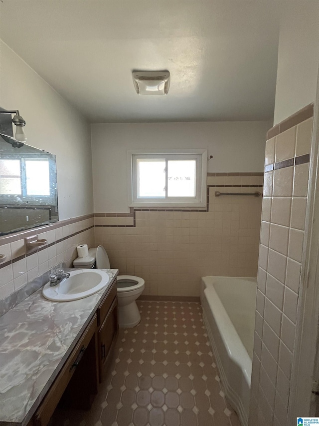 bathroom featuring a washtub, tile walls, toilet, wainscoting, and vanity