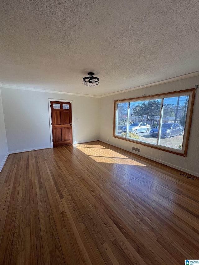 empty room featuring ornamental molding, visible vents, a textured ceiling, and wood finished floors
