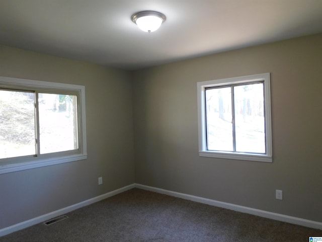 unfurnished room with baseboards, visible vents, dark colored carpet, and a wealth of natural light