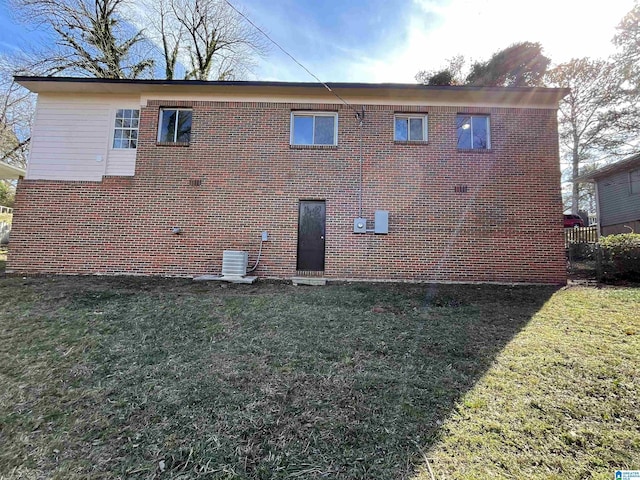 rear view of property featuring cooling unit, a lawn, and brick siding