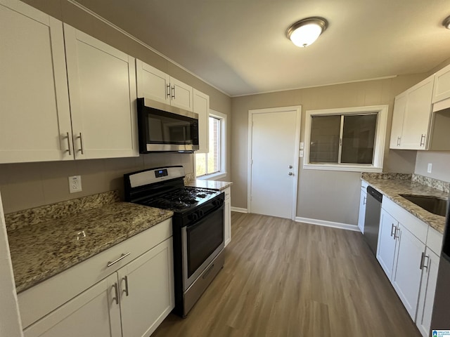 kitchen with stainless steel appliances, wood finished floors, white cabinetry, baseboards, and light stone countertops