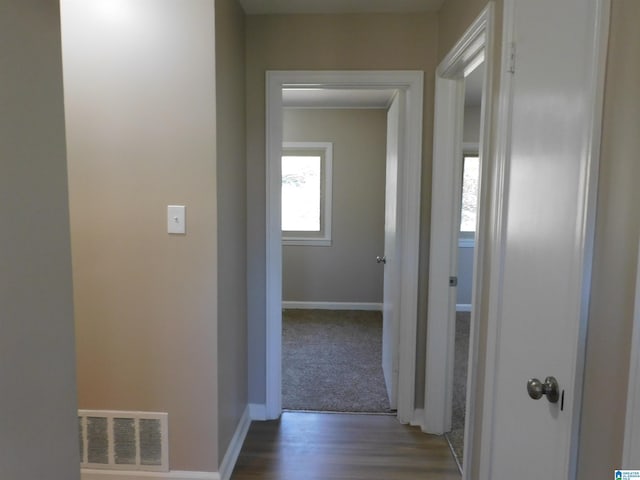 corridor featuring visible vents, baseboards, and wood finished floors