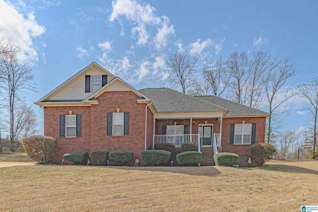 view of front of home with roof with shingles, a front yard, a porch, and brick siding