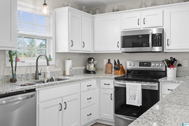 kitchen featuring light stone countertops, stainless steel appliances, hanging light fixtures, white cabinetry, and a sink