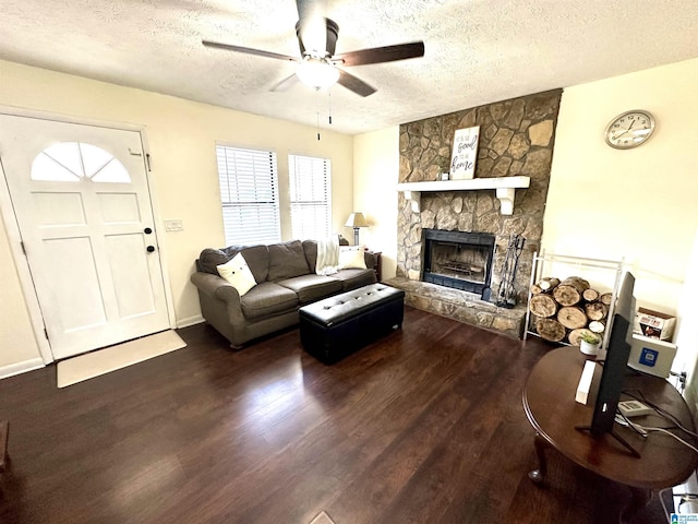 living area featuring a textured ceiling, ceiling fan, a stone fireplace, and wood finished floors