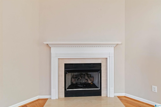 interior details featuring a fireplace with flush hearth, baseboards, and wood finished floors