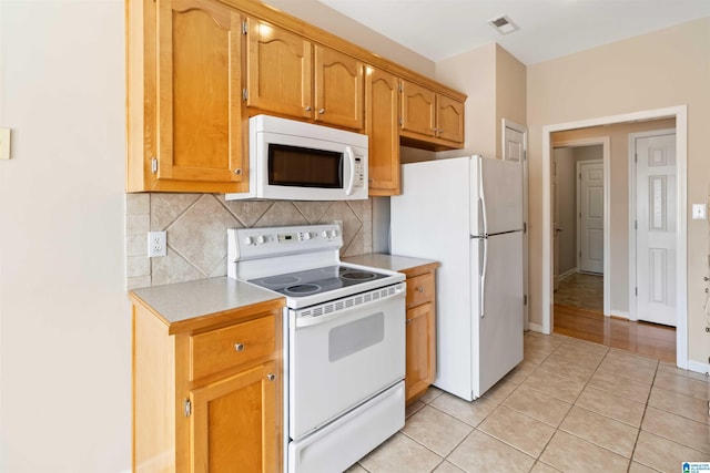 kitchen with light tile patterned floors, tasteful backsplash, light countertops, white appliances, and baseboards