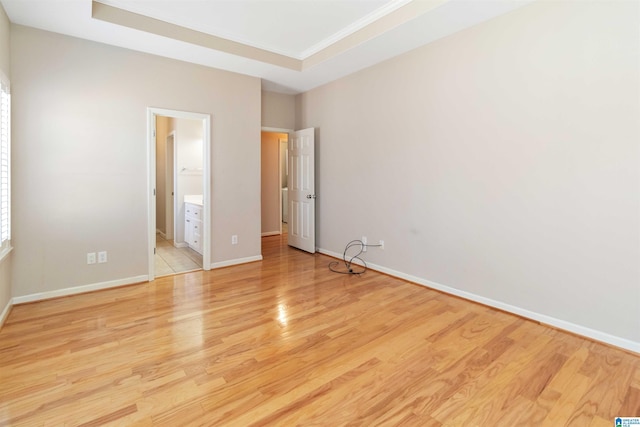 unfurnished bedroom with light wood-type flooring, baseboards, ensuite bath, and a tray ceiling