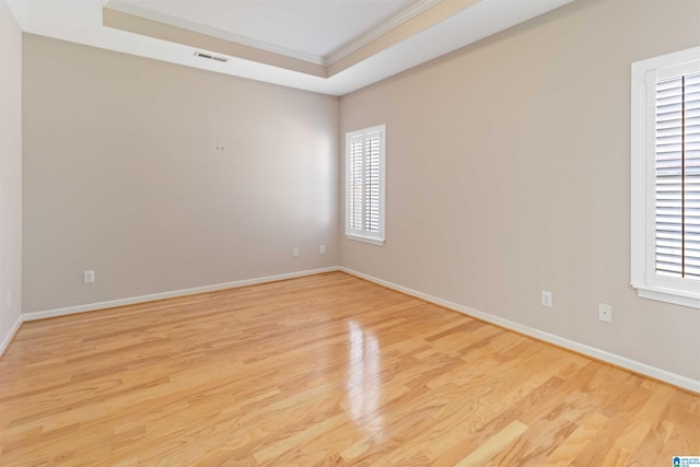 spare room with light wood-type flooring, baseboards, visible vents, and a tray ceiling