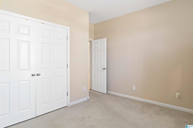 unfurnished bedroom featuring a closet, light colored carpet, and baseboards