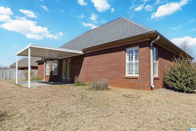 rear view of property featuring a patio, brick siding, a shingled roof, fence, and a lawn