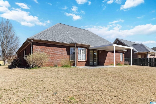 rear view of property featuring a yard, a shingled roof, fence, and brick siding