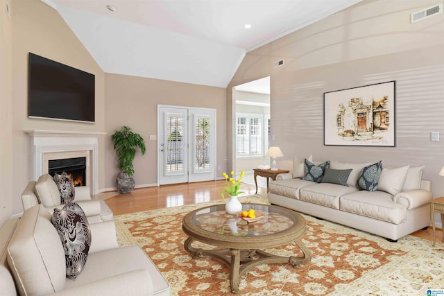 living area featuring a warm lit fireplace, wood finished floors, visible vents, baseboards, and vaulted ceiling