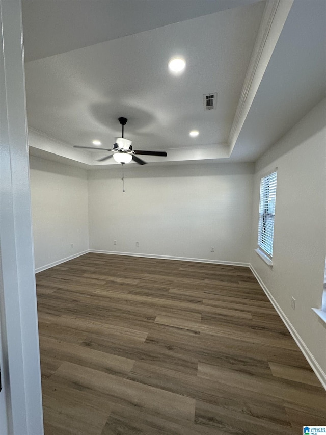 empty room featuring a raised ceiling, visible vents, dark wood finished floors, and baseboards