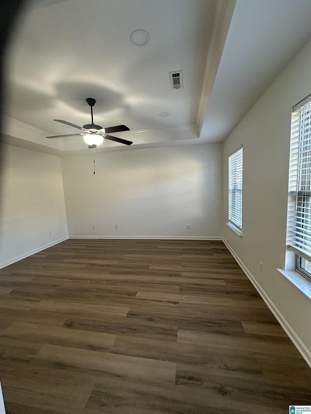 spare room featuring baseboards, visible vents, a raised ceiling, ceiling fan, and dark wood-type flooring