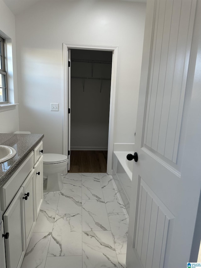 bathroom with marble finish floor, vanity, toilet, and a bath