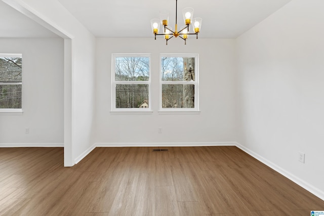 unfurnished dining area with a chandelier, visible vents, baseboards, and wood finished floors