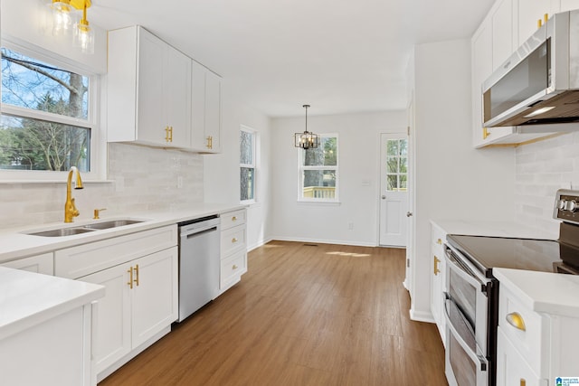 kitchen with light wood finished floors, stainless steel appliances, light countertops, white cabinets, and a sink